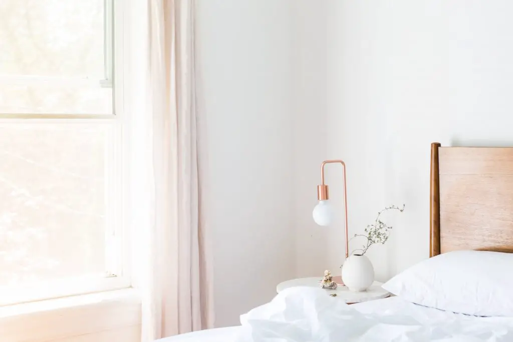 White bedroom with a rose gold bedside lamp, white bed and light pink curtains