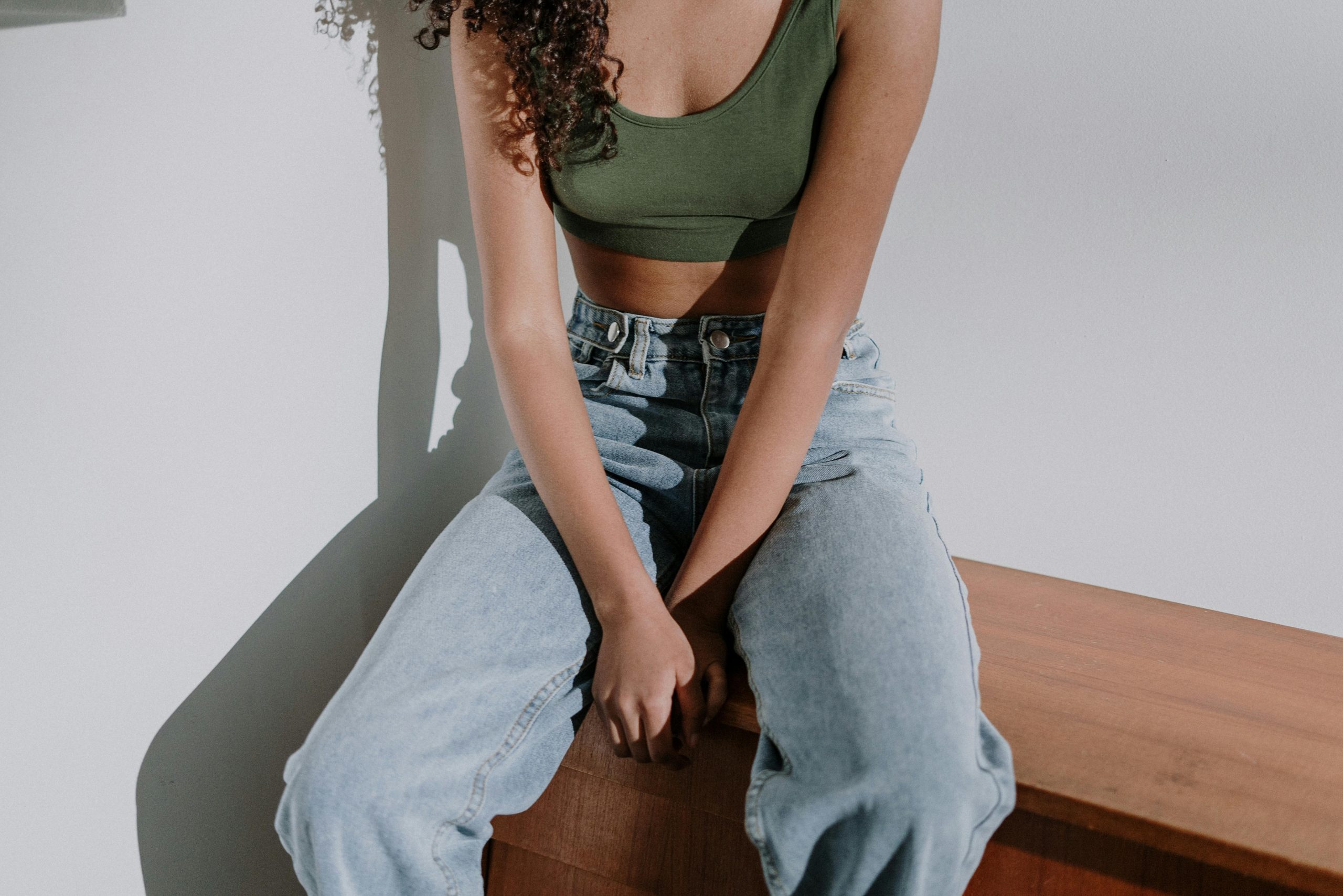 Woman in Black Tank Top and Blue Denim Jeans Sitting on Brown Wooden Bench