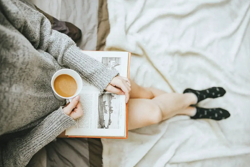 woman holding a cup of coffee whilst holding a book in other hand 