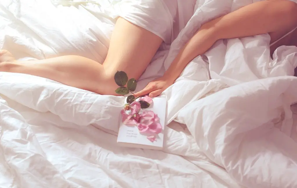 woman in white pyjamas lying on bed holding pink flower