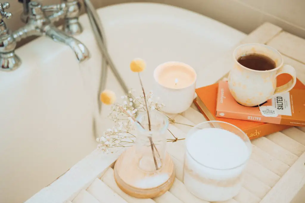 Bath tray with a cup of coffee, books, candle and flowers