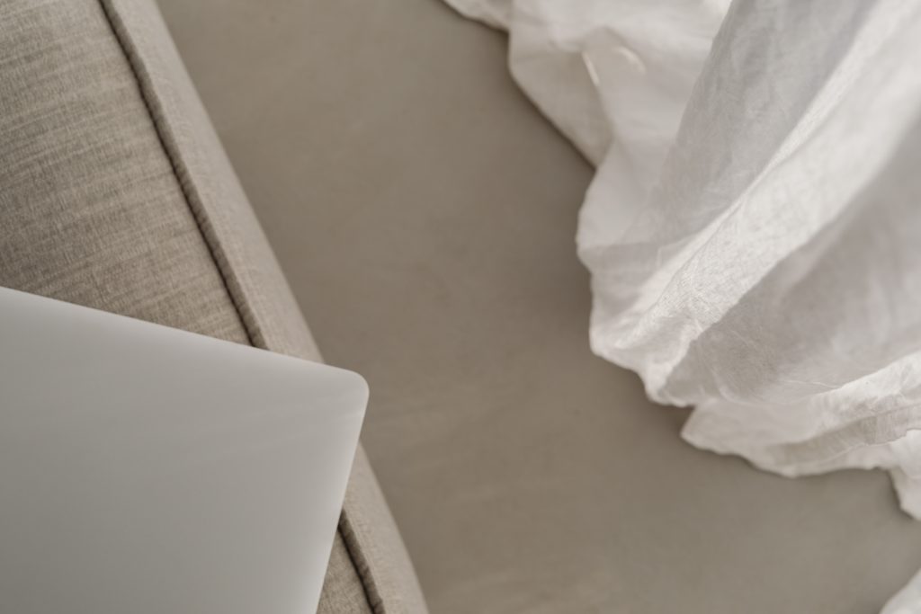 corner of laptop on sofa beside flowy curtain