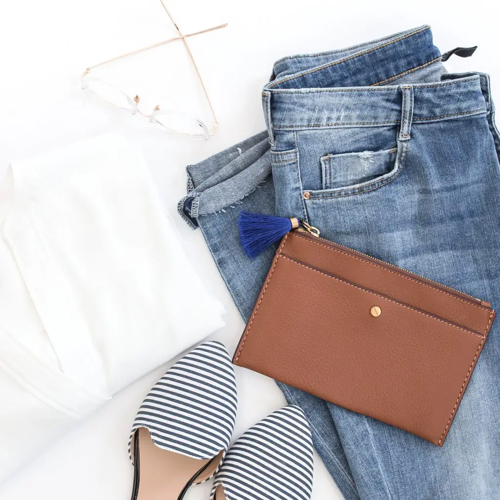 brown leather bag besides white shirt and black and white striped shoes on top of blue denim jeans