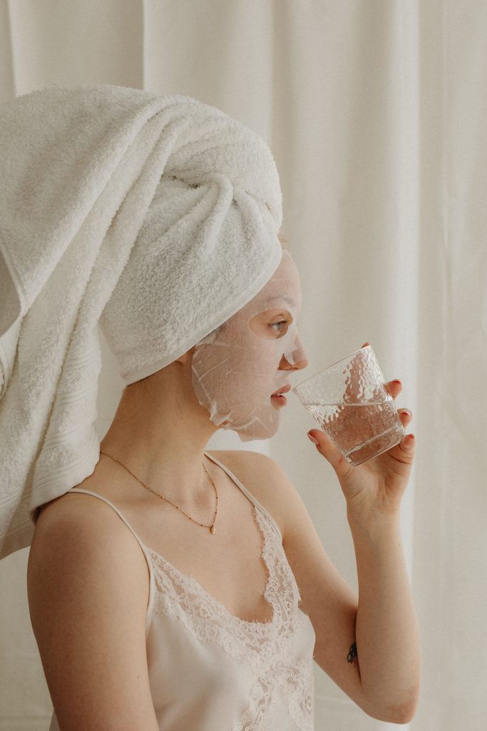 woman with sheet mask on face drinking water