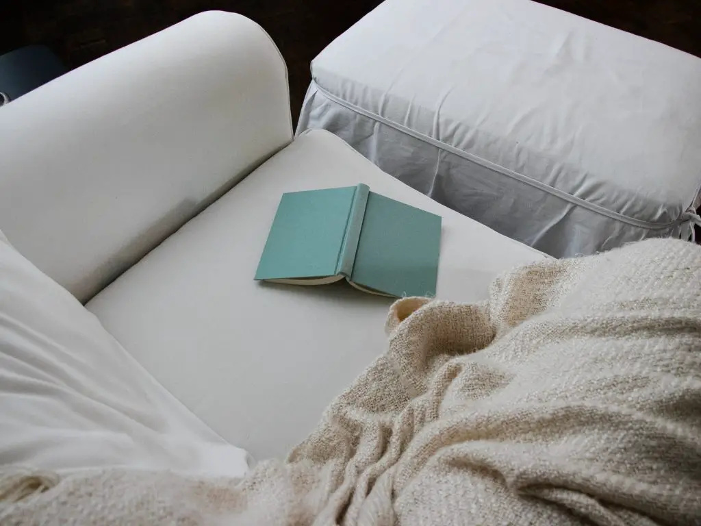 blue book on white couch beside blanket