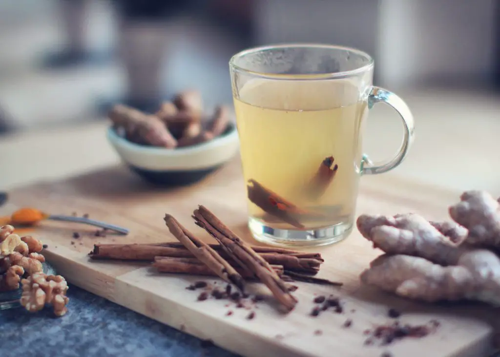 glass mug of tea beside ginger and cinnamon sticks