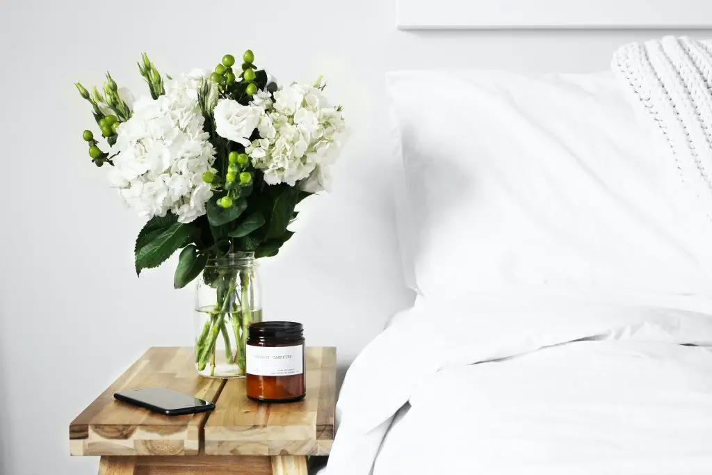 flowers, phone and candle on wooden bedside table