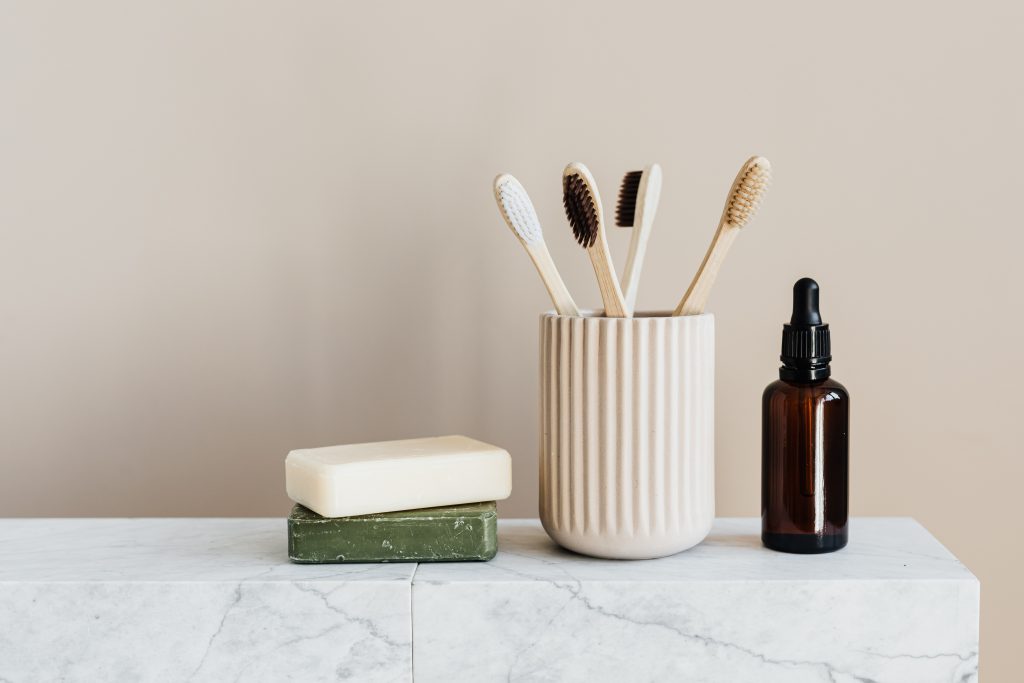 toothbrushes in brown cup beside soap and brown glass bottle