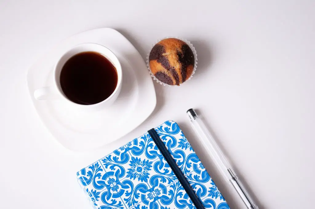 cup of coffee beside cake and notebook