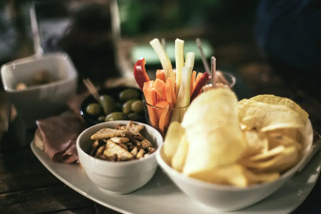 bowl of potato chips beside olives and other snacks