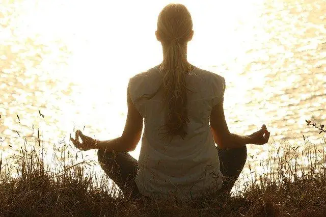 woman in sitting in yoga pose in front of lake