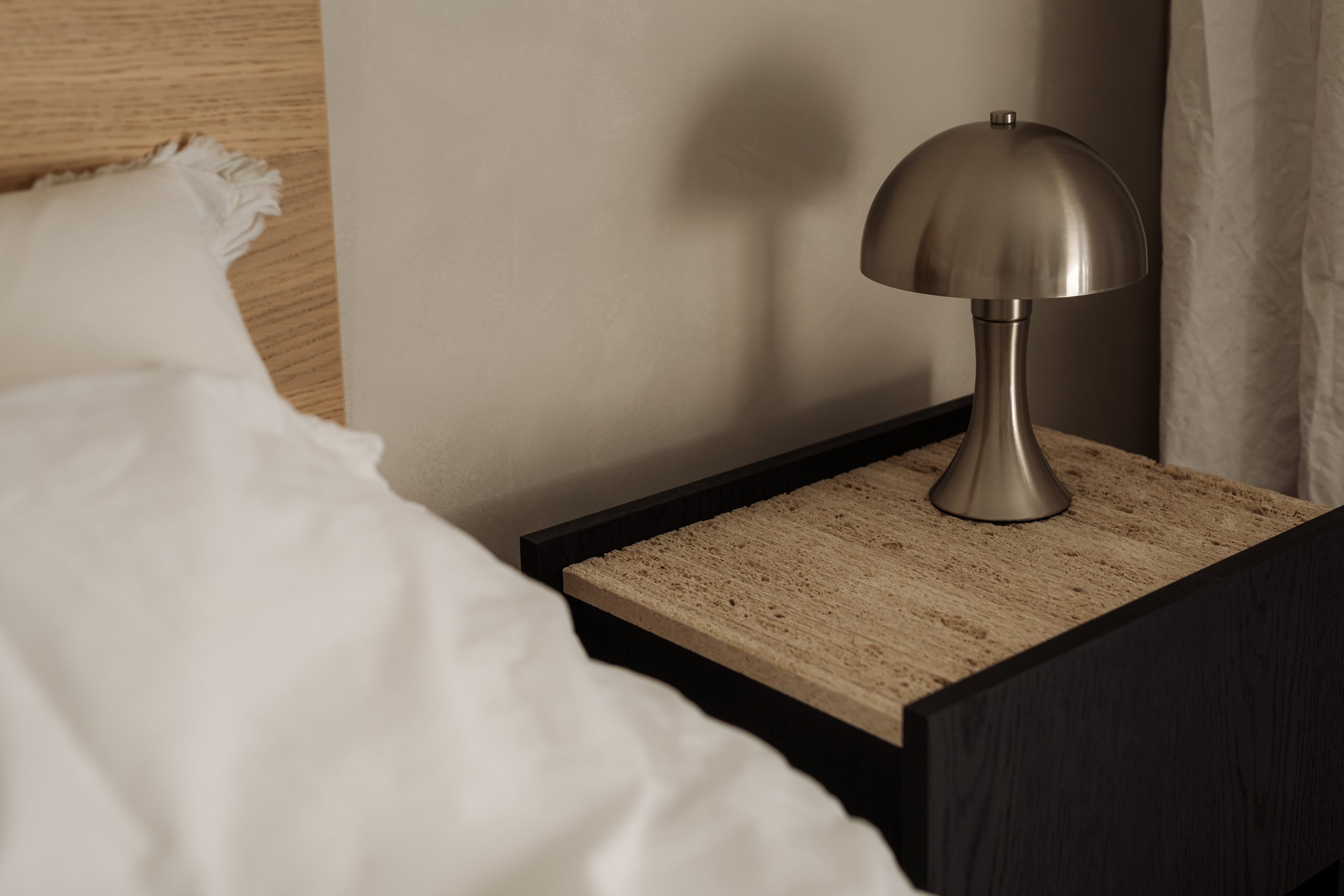 black and woond sise table beside neutral bed with white sheets