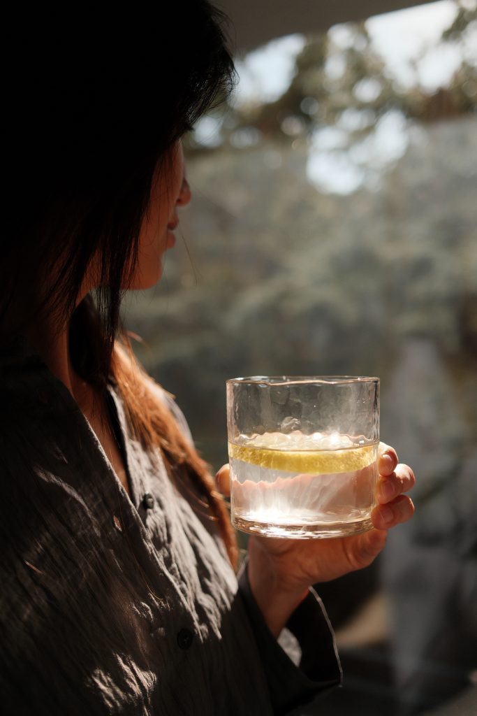 woman looking out of window holding glass of lemon water