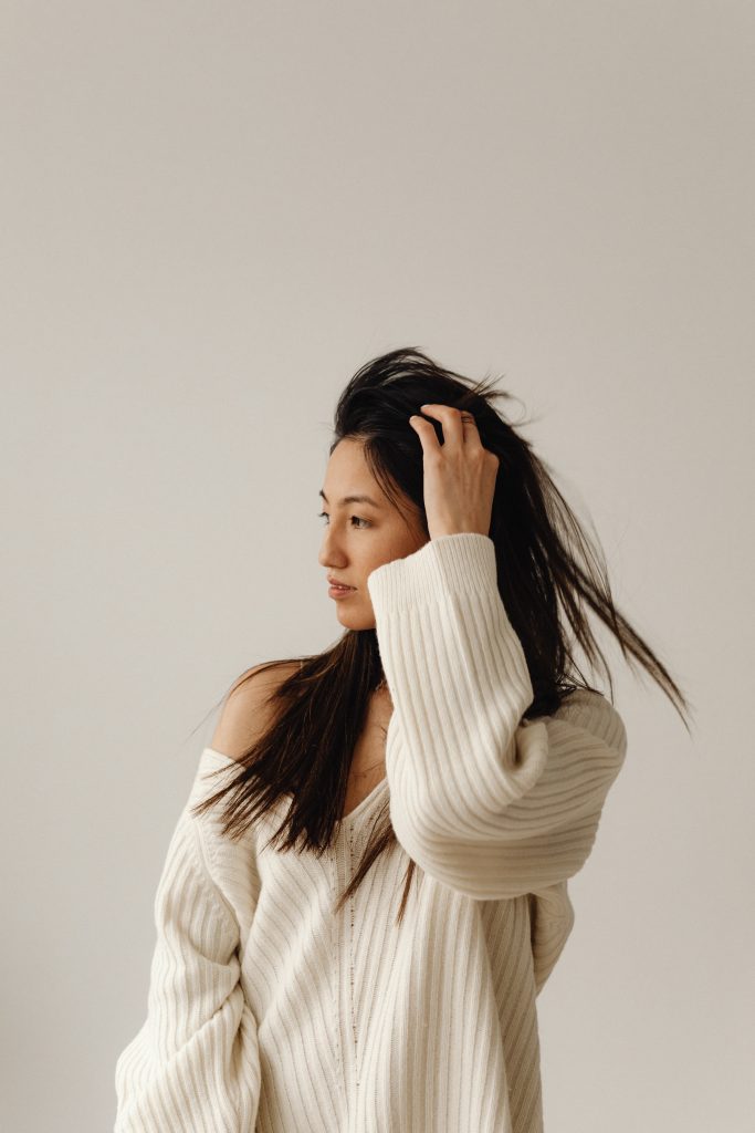WOMAN IN CREAM SEATER STANDING AGAINST GREY BACKGROUND