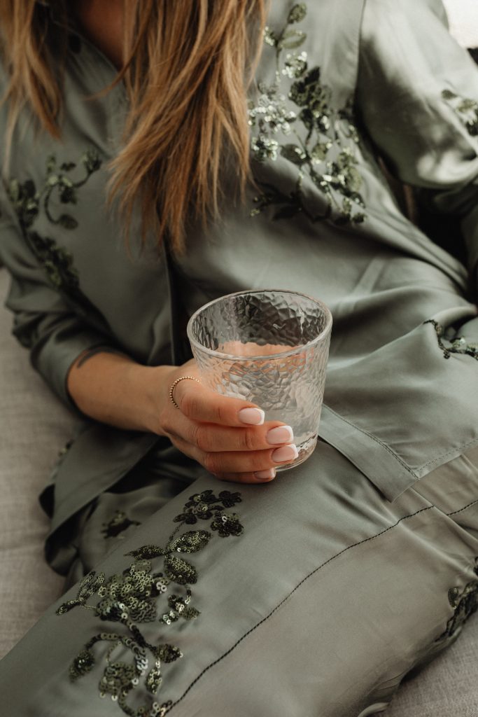 woman in green top with french manicure holding empty glass