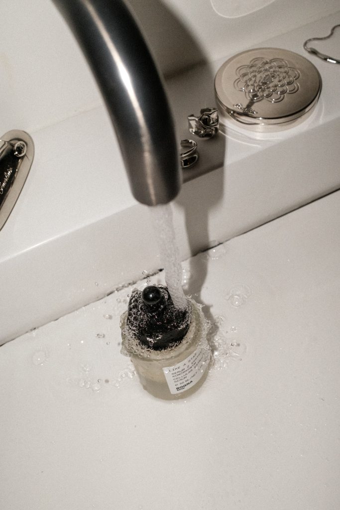 running water over perfume bottle in sink