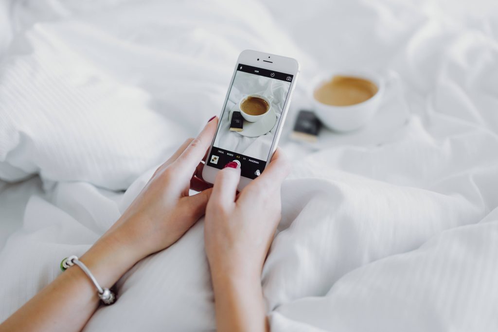 WOMAN HOLDING PHONE WITH COFFEE IN BED
