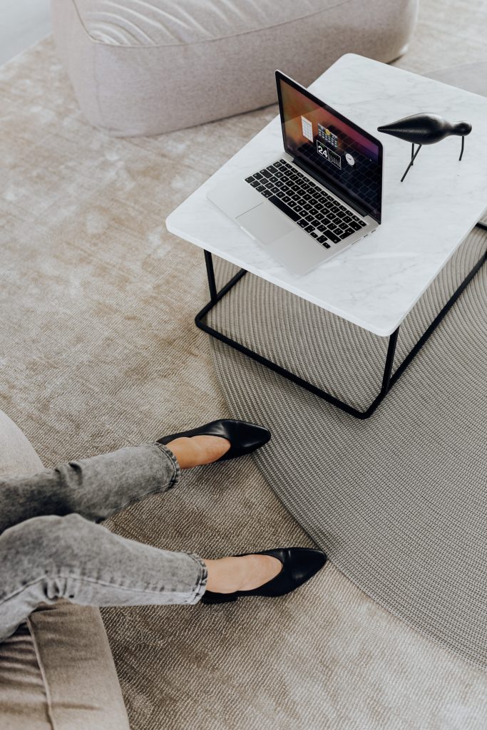 woman wearing grey jeans and black heels in front og laptop on white coffee table