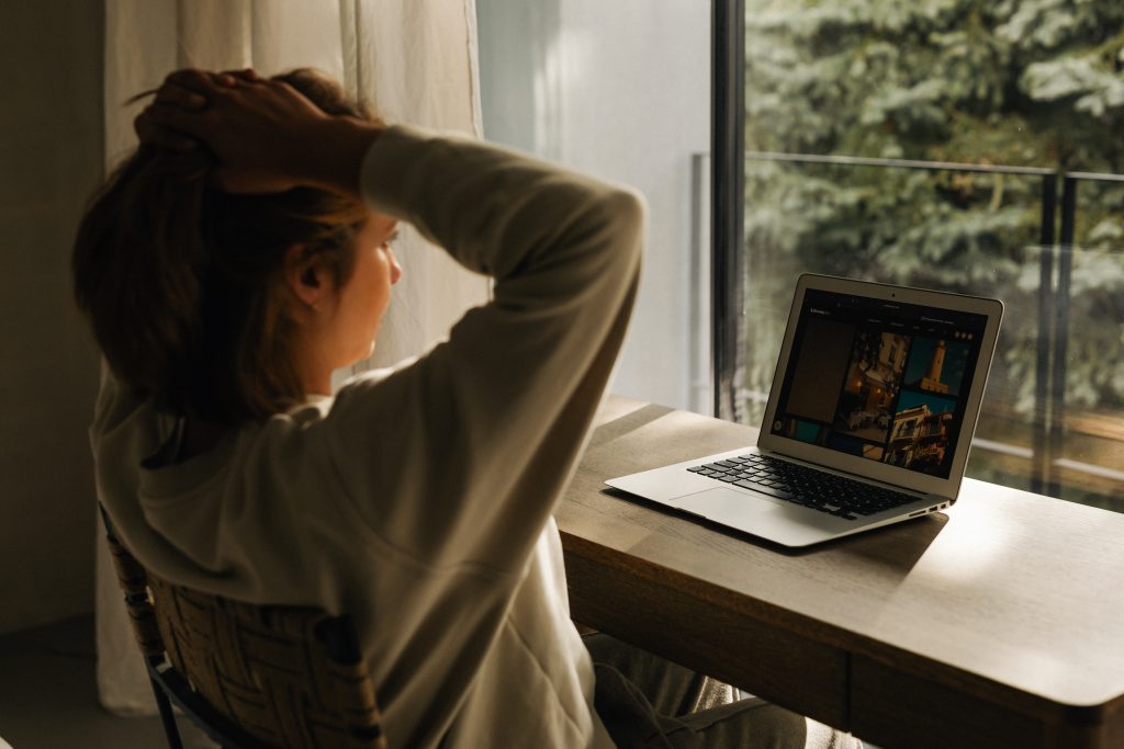 WOMAN WITH HANDS ON HEAD AT DESK LOOKING OUT WINDOW