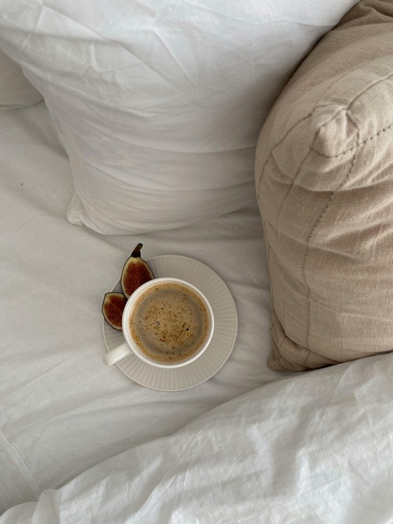 low-energy habits, cup of coffee on white bed sheets beside brown cushion